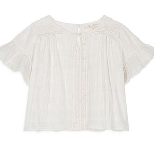 The Girls' Feliza Blouse by Louise Misha is an elegant white summer top with a round neck, delicate lace trim, and pleated detailing. Crafted from lightweight cotton and lace fabric, it features short sleeves and a back button closure for an effortlessly chic look.