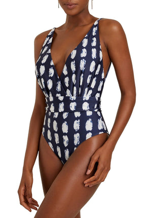 A woman models the Rec Cachecoeur One Piece by Lenny Niemeyer, a navy blue swimsuit with white abstract spots, deep V-neckline, wide waistband detail, and BIO Lycra fabric for UV protection.
