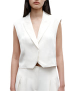 A woman wears the TWP Katie Cropped Tailored Vest, a sleeveless white blazer in European flax linen, paired with matching high-waisted pants against a plain white background.