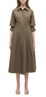 A person faces forward wearing the Simkhai Signature Jazz Dress, an olive green cotton poplin collared midi with an A-line silhouette and flared skirt, styled with beige sandals against a plain white background.
