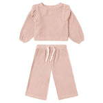The Quincy Mae Baby Girl's and Girls' Ruffle Cozy Set is a light pink two-piece ribbed knit outfit featuring a long sleeve top with ruffle details and matching wide leg pants with a drawstring waist.