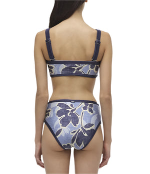 A person wears Simkhai's Luthea Tube Top and Dallia Bottom, presenting a chic blue floral print bikini with a tube-style top and high-waisted bottoms from behind.