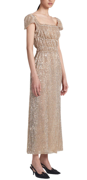 The person is elegantly dressed in an Altuzarra Lily Dress, a sleeveless, ankle-length wonder with sequin embellishments and an elasticated waist, complemented by sleek black heeled shoes.