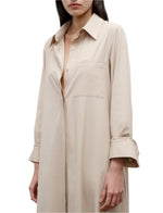 A woman wears Jenny's Crystal Gown by TWP, an oversized maxi shirt dress in Italian cotton shirting with partially undone buttons and cuffed sleeves.