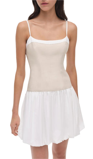 A woman wears the Simkhai Fifi Mini Dress, a sleeveless linen poplin dress with thin straps, a fitted beige bodice, and a white gathered bubble skirt.