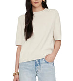 A person wearing the Anine Bing Jackson Sweater, a short-sleeved crewneck in cream, paired with light blue jeans and one hand in their pocket.