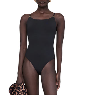 A person wears the Anine Bing Vesta One Piece, a black minimalist swimsuit with adjustable straps, and holds a leopard print garment in one hand against a white background.