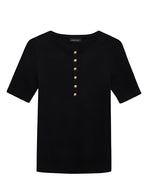 The Alessia Tee by Anine Bing is a black short-sleeve Henley with a round neck, featuring six gold buttons. Made from a cotton-spandex blend, it has a subtle ribbed texture for style and comfort.