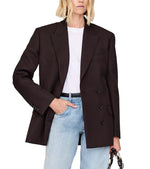 A woman wears the Aretha Blazer by Anine Bing—a slim hourglass-fit tuxedo wool blazer with a notched collar—over a white t-shirt and light blue jeans, with one hand in her pocket and the other holding a small bag.