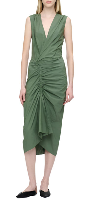 A person looks elegant in the Agnes Dress by Callas Milano, a sleeveless green wrap dress with a ruched front and V-neck, made of fine Italian cotton, stylishly paired with black flats.