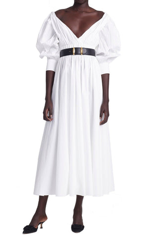 The person is wearing the Altuzarra Kathleen Optic White Dress, featuring a V-neck and puffed sleeves, cinched with a black belt, and paired with sleek black heels.
