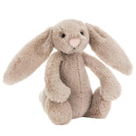 The Jellycat Bashful Beige Bunny, Small, features long floppy ears, a pink nose, and soft beige fur. Sitting upright against a white background, it makes an adorable plush gift for any occasion.