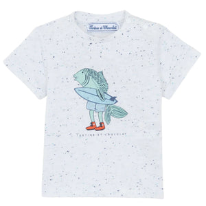 The Baby Boys' and Boys' Surfer Fish Tee by Tartine et Chocolat showcases a white speckled T-shirt with a surfing fish character holding a surfboard, wearing shorts and red shoes. It subtly displays summer elegance with the brand label below.