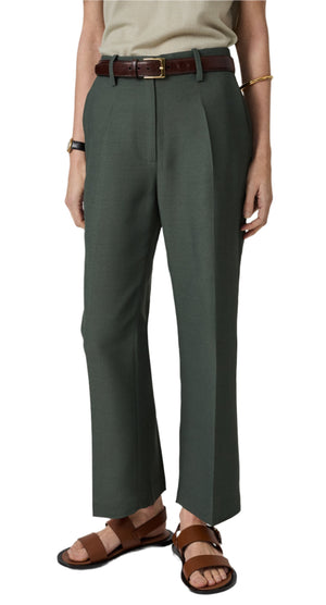 A person wears CO's Cropped Flared Pant in green, crafted from lightweight virgin wool, paired with a brown belt, an olive top, and brown sandals.