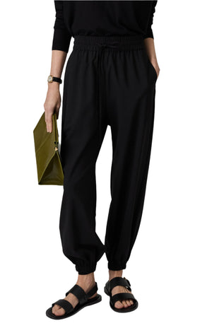 Person wearing CO Jogger Pant, a black long-sleeve top, sandals, and holding a green clutch.