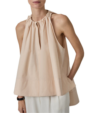 A person showcases a sleeveless, light beige Gathered Tunic Shirt from CO, made of cotton poplin, paired effortlessly with white trousers.