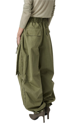 The person is wearing CO's Articulated Vented Pant in oversized olive green, made from garment dye cotton twill with an elasticized waistband and cuffs, stylishly paired with high heels for a chic look.