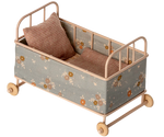 The Maileg Cot Bed, Micro – Powder is a small beige metal bed with floral fabric sides, wooden wheels, a soft mattress, and two checkered pillows—ideal for your micro sized friends.