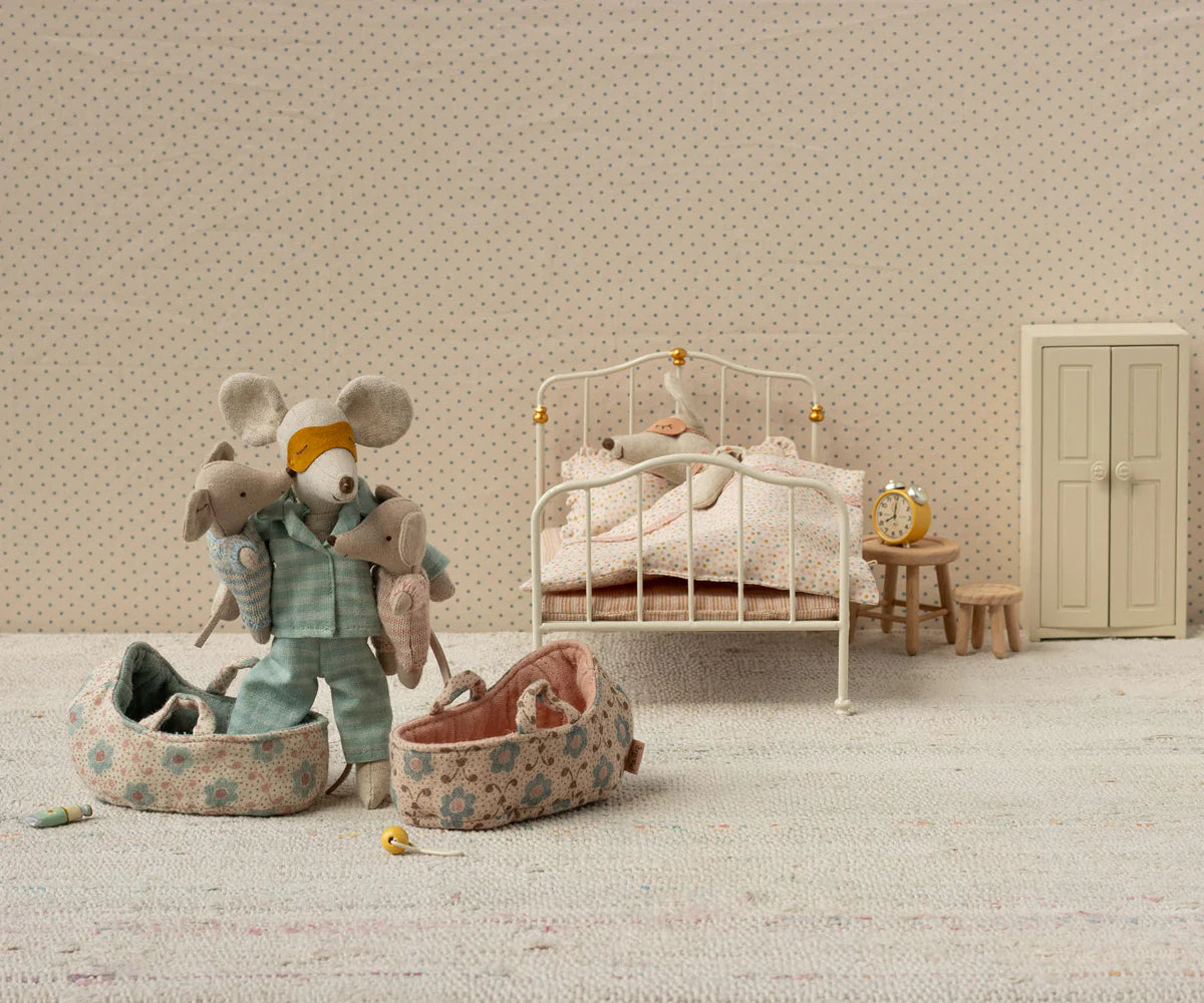 Maileg’s Baby Mouse in Carry Cot - Rose features a charming miniature bedroom scene with a mouse doll, baby mouse, bed, slippers, and nightstand with alarm clock.