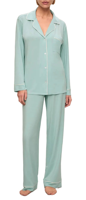 A person is wearing the Eberjey Gisele Long PJ Set, a relaxed light blue TENCEL™ Modal long sleeve top with white piping and matching full-length pants, standing barefoot.