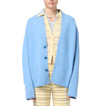 Model wears the Everywear Cardigan by Guest in Residence, a light blue oversized jacket with a shawl collar, layered over a yellow plaid shirt and matching pants, set against a white background.