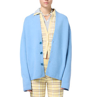 Model wears the Everywear Cardigan by Guest in Residence, a light blue oversized jacket with a shawl collar, layered over a yellow plaid shirt and matching pants, set against a white background.