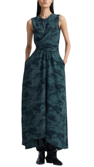 A woman in a sleeveless, dark green Altuzarra Penny dress with a nature pattern, draped front, ankle-length hem, and waist-accentuating design, paired with black boots.