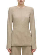 A model wears the Adam Lippes Noa Top in beige Italian tropical wool, a long-sleeve tailored style with removable shoulder pads, paired with matching pants, shown from the front against a plain white background.