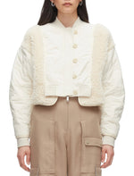 A person models the 3.1 Phillip Lim Cropped Sherpa Combo Bomber with beige cargo pants. Their long, dark hair flows freely as they face forward, effortlessly showcasing this stylish quilted jacket with faux shearling trim.