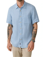 A person wears a lightweight bestseller—Faherty’s Short-Sleeve Palma Linen Shirt in light blue—with beige pants. Their tattooed arms enhance the look, and a watch adorns their left wrist.