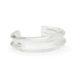 The Onda Cuff by Lizzie Fortunato is a clear, chunky glass bracelet with a sculptural design that resembles waves, viewed from a slight angle.