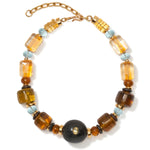 The Desert Mirage Collar by Lizzie Fortunato features gold, amber, blue, and black beads—including a bold central black bead, striking flame-worked glass accents, and an adjustable gold chain clasp.