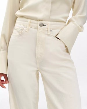A person wearing Rag & Bone’s Featherweight Logan cream-colored button-up shirt and matching wide leg jeans, with one hand in their pocket.