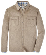 The Peter Millar Crown Flex Fleece Shirt Jacket, crafted from Merino wool, is a beige button-up featuring two chest pockets and a blue plaid lining for a lightweight wearing experience.