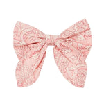 The Louise Misha Gilla Hair Clip is a pink fabric bow with a floral pattern, two wide loops, and angled tails—perfect as a charming floral accessory.