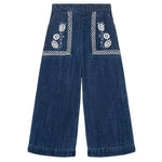 The Girls' Flofi Pants by Louise Misha are wide-leg blue denim pants with white floral embroidery, decorative front pocket stitching, and an elastic waist for comfort.