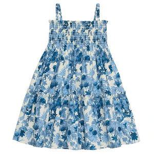 The Cara Cara Girls' Goldie Dress is a sleeveless style with a smocked top, tiered flowy skirt, and a blue and white floral print.
