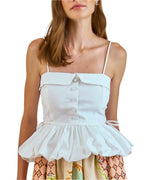 The Juliana Top by Hunter Bell NYC combines feminine charm with its white, buttoned, sleeveless design and peplum hem. Pair it effortlessly with a colorful skirt featuring geometric and floral patterns for a modern design.