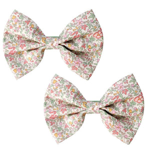 The Milledeux Girls' Large Bowtie Bow in Liberty Katie & Millie B fabric features charming floral patterns in pink, green, and orange on white, secured with grosgrain-covered alligator clips for easy styling.