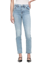 A person wearing Frame's Le High Straight Raw After light blue jeans made from sustainable stretch cotton stands in black heels with one hand in their pocket against a white background, highlighting the high-rise waist and sleek straight leg design.