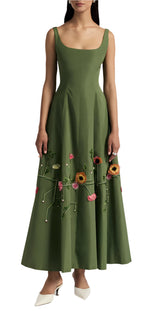 A woman in Lela Rose's Seam Detail Scoop Neck Taffeta Midi Dress, featuring a sleeveless design and colorful floral embroidery at the waist, in green, pairs elegantly with white heels.