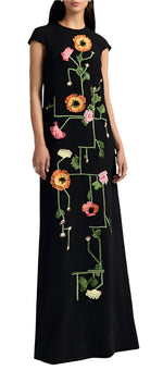A person wears the Augusta Embroidered Gown by Lela Rose, showcasing vibrant tulip fields in orange, pink, and green against a long black dress. The gown's silhouette beautifully highlights its exquisite floral embroidery.