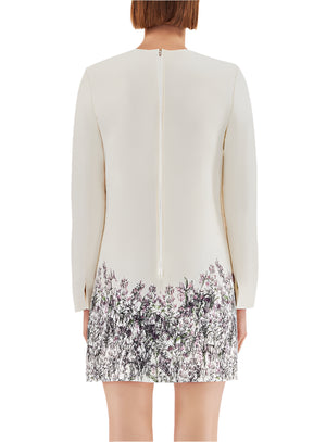 A back view shows a person with shoulder-length hair wearing the Tilley Silk Wool Dress by Adam Lippes, a cream-colored, long-sleeve dress with floral print on the lower half and a center zipper. The midi-length design complements their look beautifully.