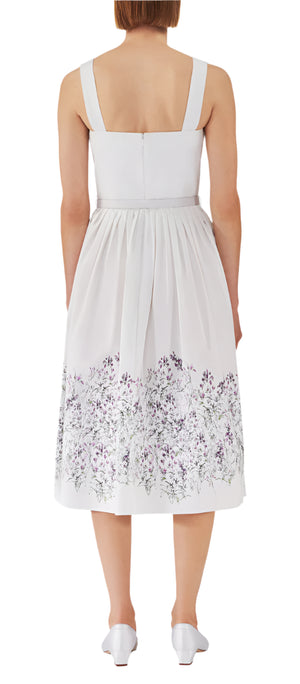 A person is seen from the back on a white backdrop, wearing a sleeveless Adam Lippes Hoban Dress with poplin fabric and floral hem patterns.
