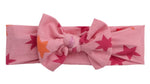 The Baby Girls' Cosmic Confetti Bow Headband by Magnetic Me is a pink modal headband with red and orange star patterns—a delightful accessory for your little one.