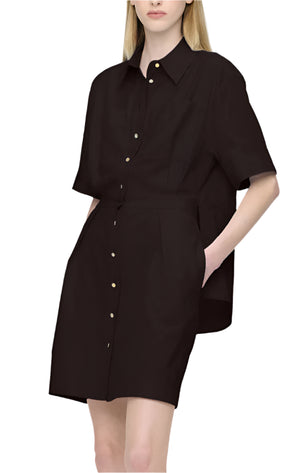 Someone is wearing the Montana Dress by Callas Milano, a black short-sleeved shirt dress made with Italian Albini fabric and button details. Hands rest casually in pockets against a plain white background.
