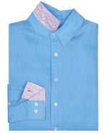 The Pink House Mustique Mens' Solid Linen Shirt in light blue features a pink patterned inner collar and cuff, neatly folded and displayed against a white background.