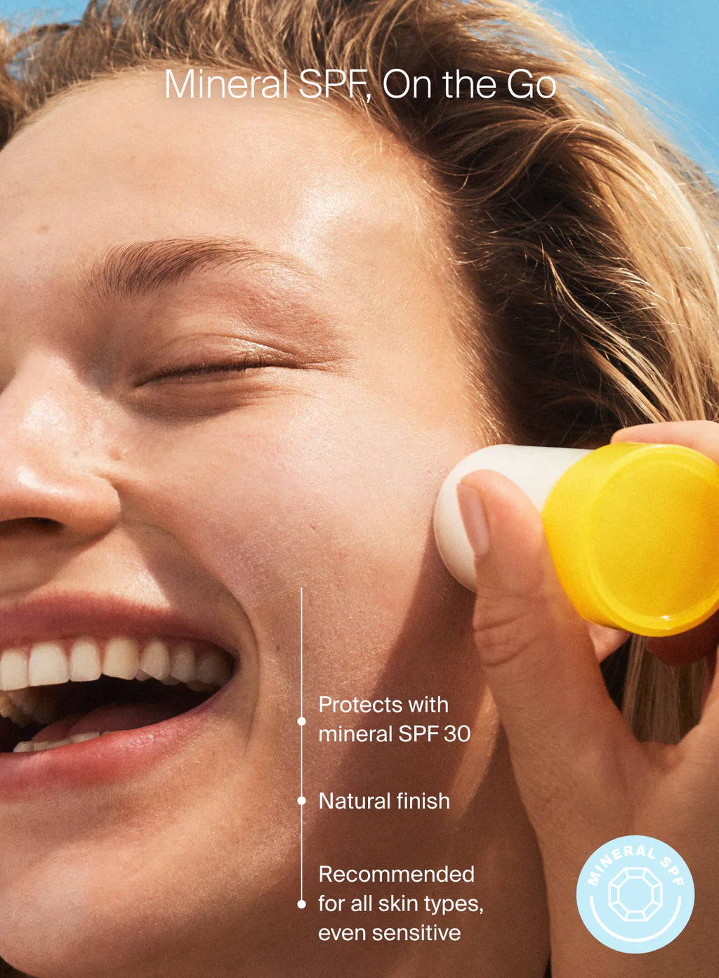 A person smiles while applying Supergoop Mineral Sheer Stick SPF 30 to their cheek; text notes its sheer, natural finish formula suitable for all skin types, even sensitive.