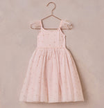 A Girls' Poppy Dress from Noralee, pale pink with spaghetti straps and a tulle skirt overlay adorned with small dot patterns, hangs on a metal hanger against a light background.