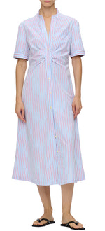 A person wearing the Noor Dress, a blue and red striped midi-length shirt dress with short sleeves by Callas Milano, paired with black flip-flops.